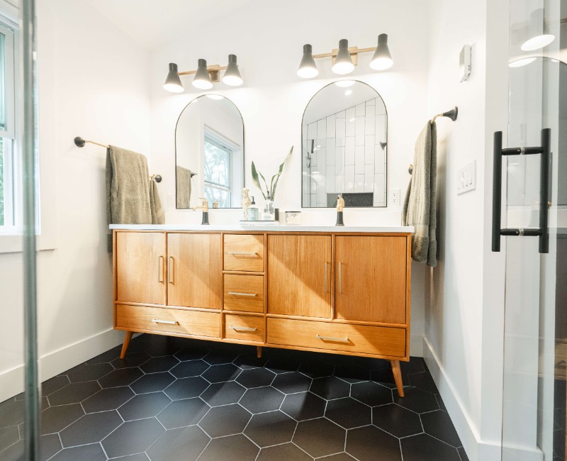 A bold black-and-white ensuite bath with frameless glass, warm wood cabinetry, and a custom sliding door — part of a NARI award-winning attic conversion by Chads Design Build in Madison, WI.