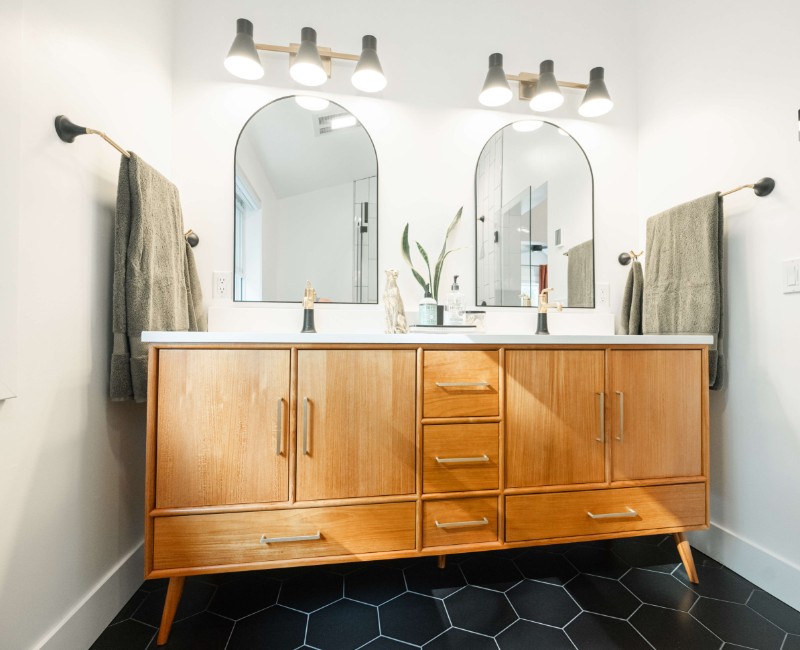 A bold black-and-white ensuite bath with frameless glass, warm wood cabinetry, and a custom sliding door — part of a NARI award-winning attic conversion by Chads Design Build in Madison, WI.