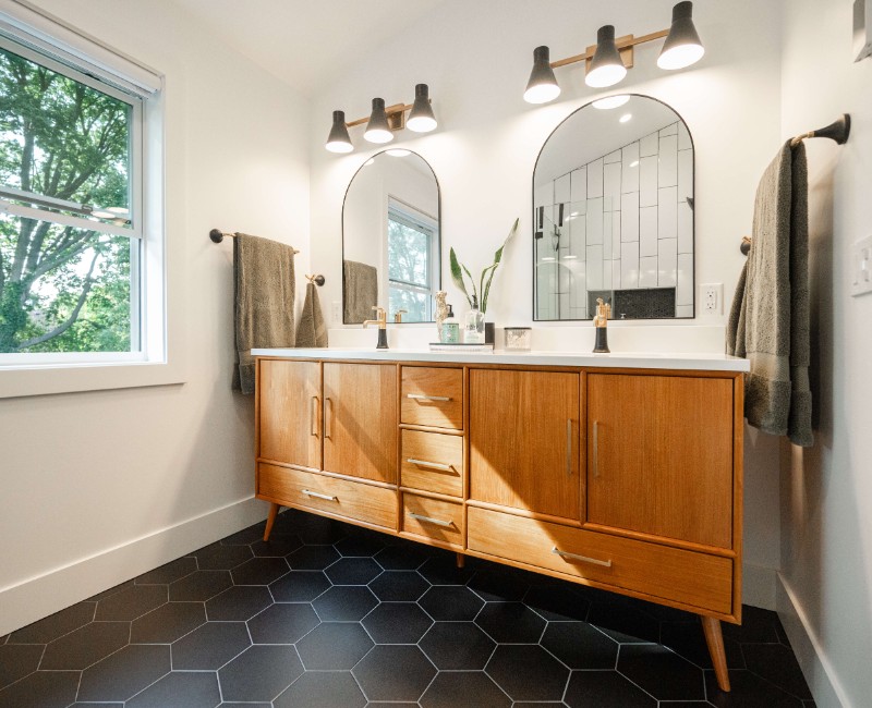 A bold black-and-white ensuite bath with frameless glass, warm wood cabinetry, and a custom sliding door — part of a NARI award-winning attic conversion by Chads Design Build in Madison, WI.
