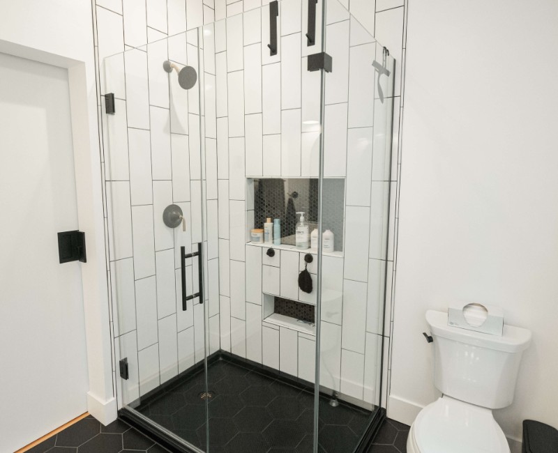 A bold black-and-white ensuite bath with frameless glass, warm wood cabinetry, and a custom sliding door — part of a NARI award-winning attic conversion by Chads Design Build in Madison, WI.