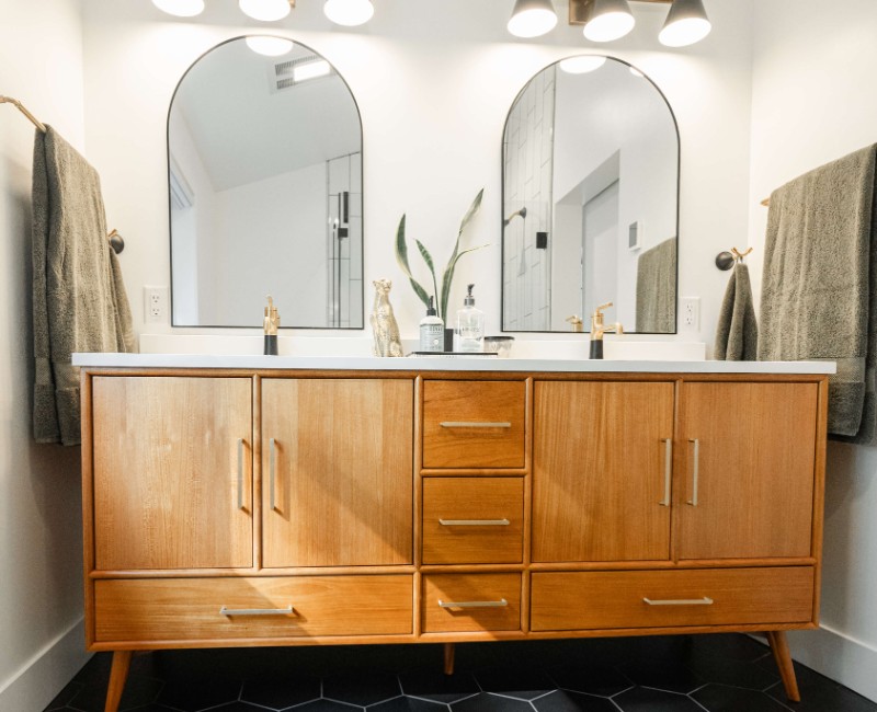A bold black-and-white ensuite bath with frameless glass, warm wood cabinetry, and a custom sliding door — part of a NARI award-winning attic conversion by Chads Design Build in Madison, WI.