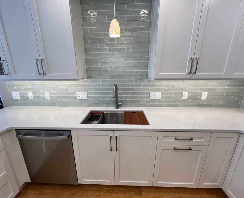 We remodeled this kitchen in Madison, WI to be bright and functional. Our team adjusted the layout, installed bamboo flooring, and added a peninsula. We installed white linen cabinets, white marble countertops, and a blue/gray tile backsplash to finish the look.