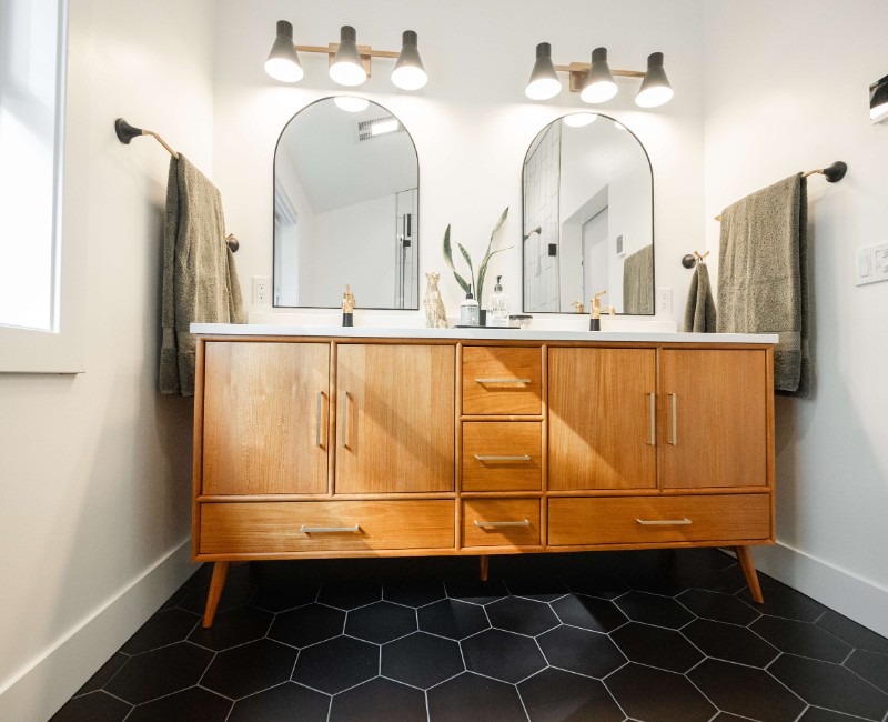A bold black-and-white ensuite bath with frameless glass, warm wood cabinetry, and a custom sliding door — part of a NARI award-winning attic conversion by Chads Design Build in Madison, WI.